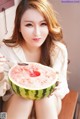 A woman holding a slice of watermelon with a spoon in it.